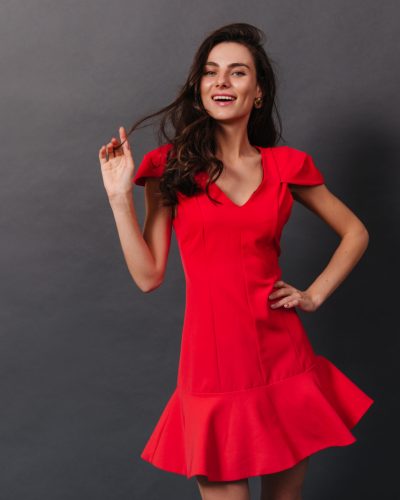 Fragile lady with dimpled cheeks smiles. Lady in red dress smiles and plays hair on black background